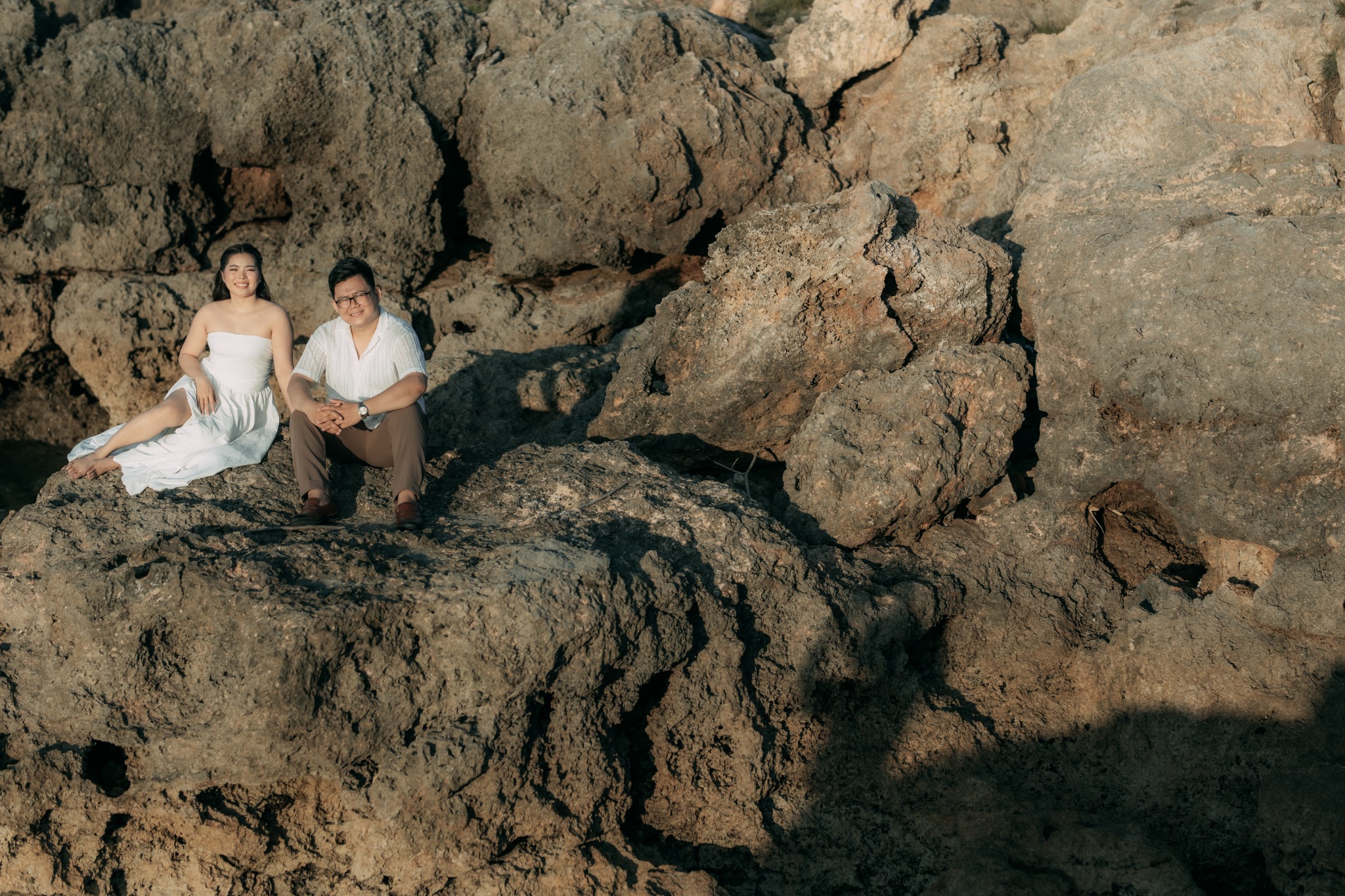 The couple seated by coastal rocks
